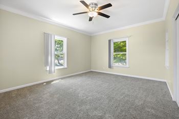 A room with a ceiling fan and two windows.